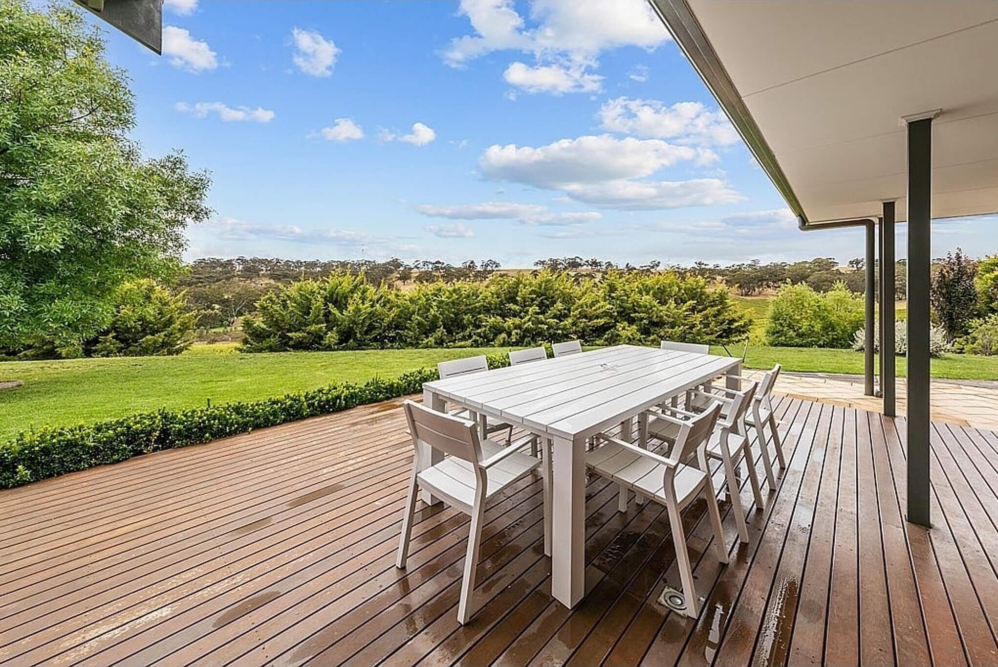 A wooden deck with a white table and chairs, overlooking a lush green landscape and hills.