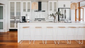 A modern kitchen with white cabinetry, a herringbone backsplash, a central island with bar stools, and a gas stove. - Skillogalee Estate (Spring Gully)