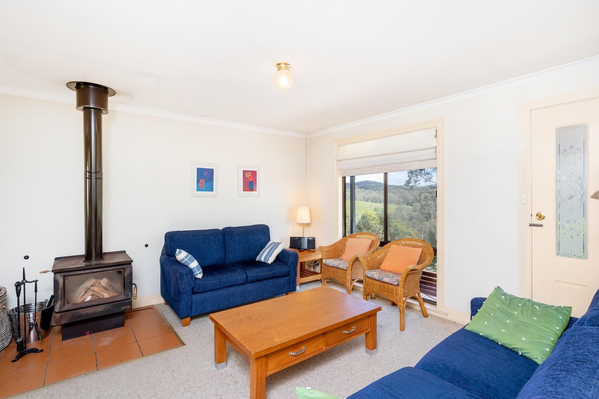 A cozy living room with a wood-burning stove, blue sofas, a wooden coffee table, and a wicker chair.