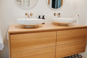 A bathroom with two white vessel sinks, wooden vanity, and two round mirrors.