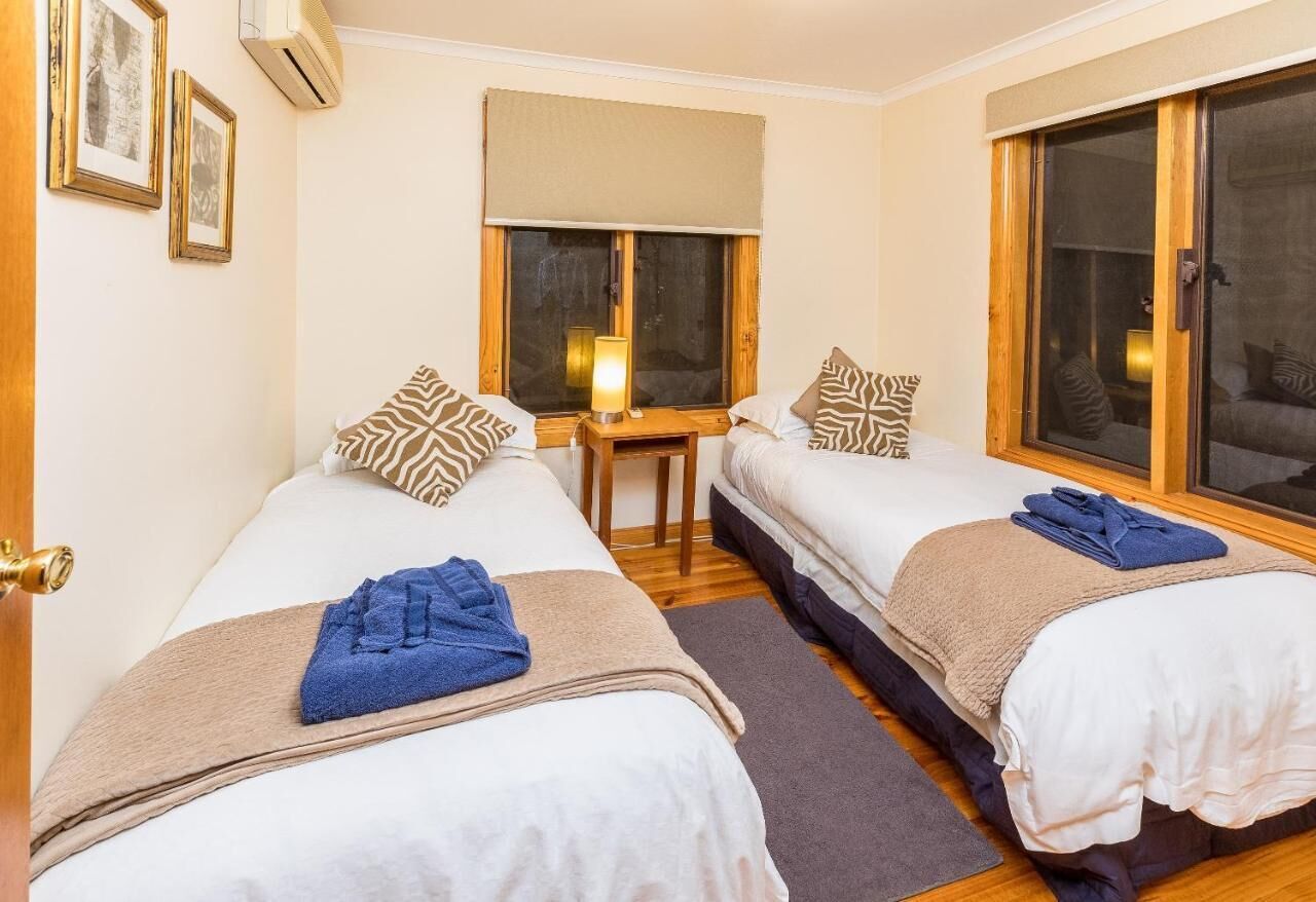 A hotel room with two beds, a small table, and a window with a view.