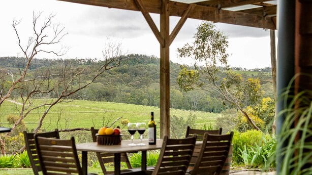 A table set outdoors with chairs, a bottle of wine, and a bowl of fruit. - Skillogalee Estate (Spring Gully)