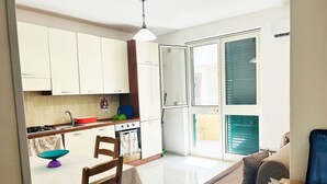 Cocina compacta con armarios blancos, estufa y comedor con mesa y sillas.