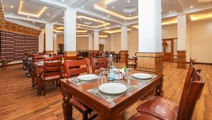 Een ruime eetruimte met houten tafels en stoelen, een centrale kolom en een decoratieve wand.