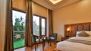 Een hotelkamer met een groot bed, een bureau met stoel en een balkon met uitzicht op groen.