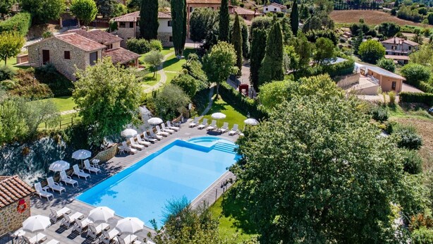 A pool area with lounge chairs and umbrellas, surrounded by greenery and stone buildings. - Agriturismo Case Graziani - Molino (Citta della Pieve)