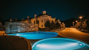Une piscine illuminée la nuit, avec un mur en pierre et un bâtiment en arrière-plan.