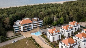 Un hôtel à plusieurs étages doté d’une piscine, entouré d’une zone boisée et situé près d’une plage.