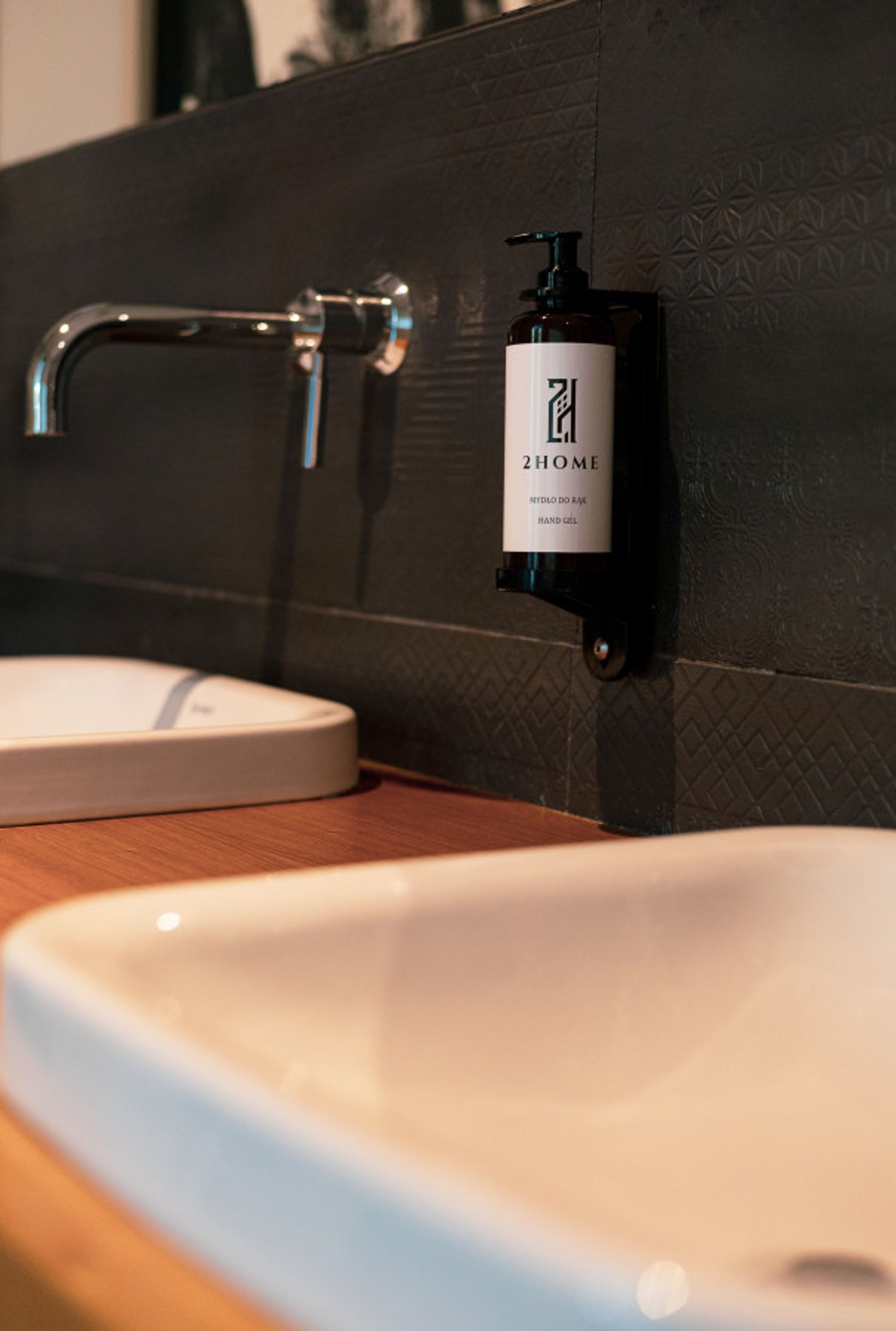 Ein Badezimmer mit einem weißen Waschbecken, einem schwarzen Seifenspender und einem modernen Wasserhahn.