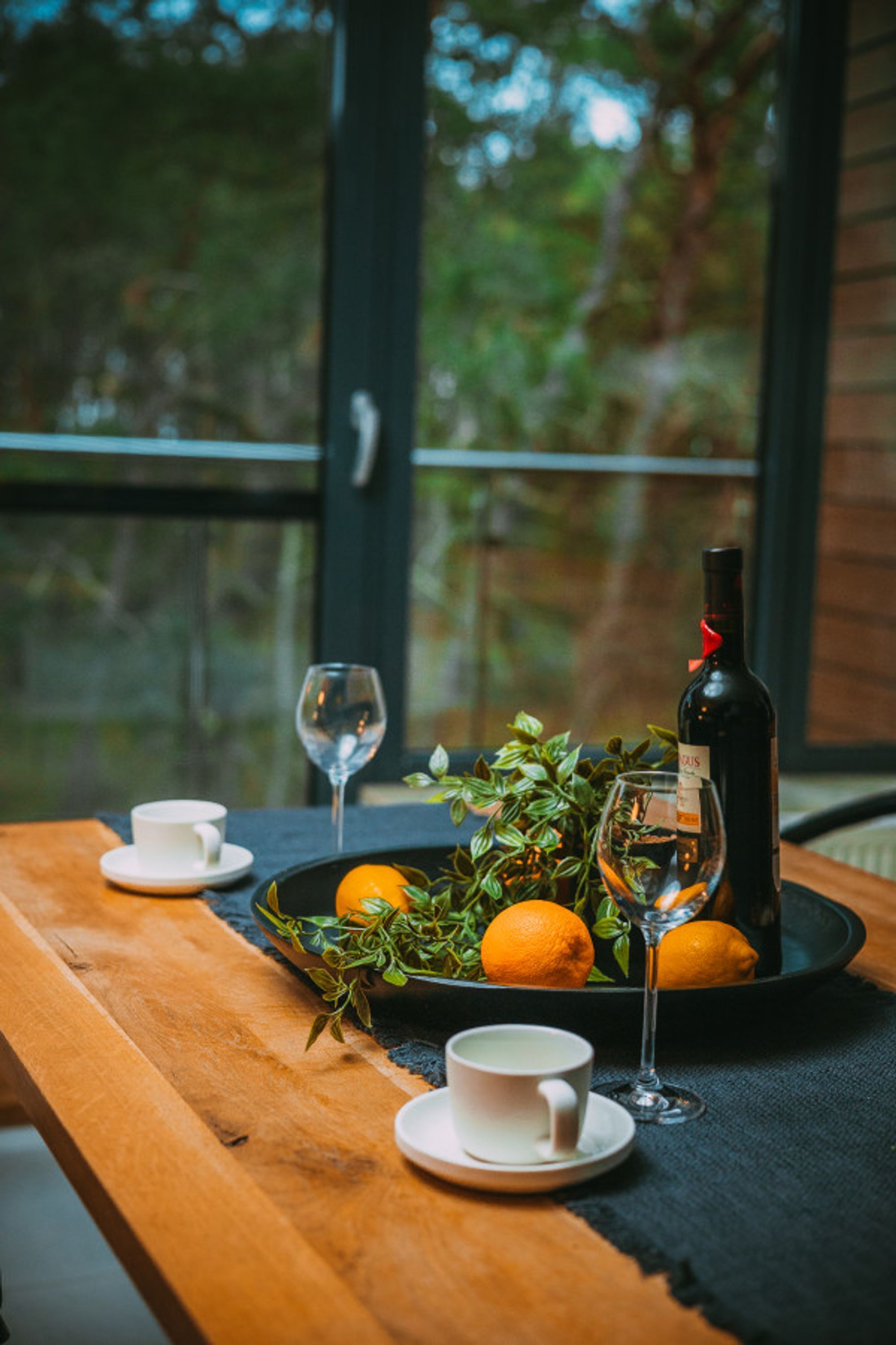 A wooden table with a tray containing oranges, a bottle of wine, and two glasses.