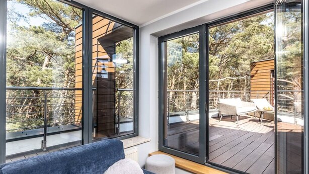 Une chambre moderne avec de grandes fenêtres, un canapé bleu et une vue sur une terrasse extérieure avec une table et des chaises.