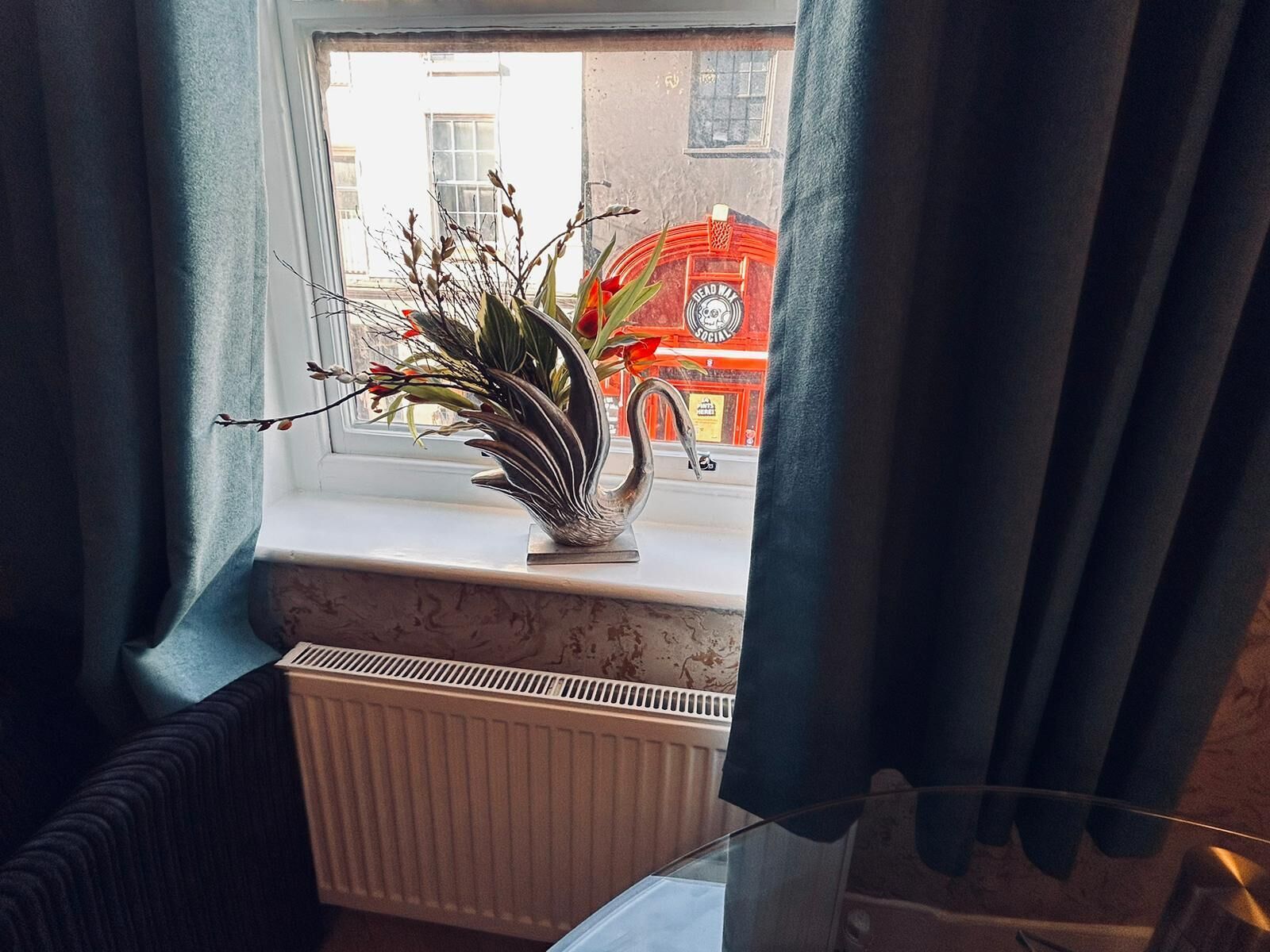 Una ventana con una planta en el alféizar, un radiador debajo y un edificio rojo en el exterior.