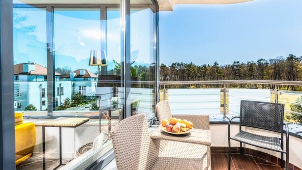 A balcony with wicker furniture, a table with fruit, and a view of buildings and trees. - Safari Relaks i Aktywny Wypoczynek Idealna Lokalizacja (Trzebiatow)