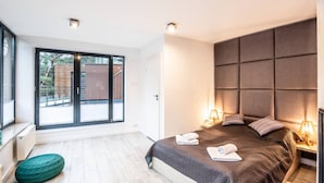 Ein modernes Schlafzimmer mit einem großen Bett, einem grünen Hocker und Blick ins Freie.