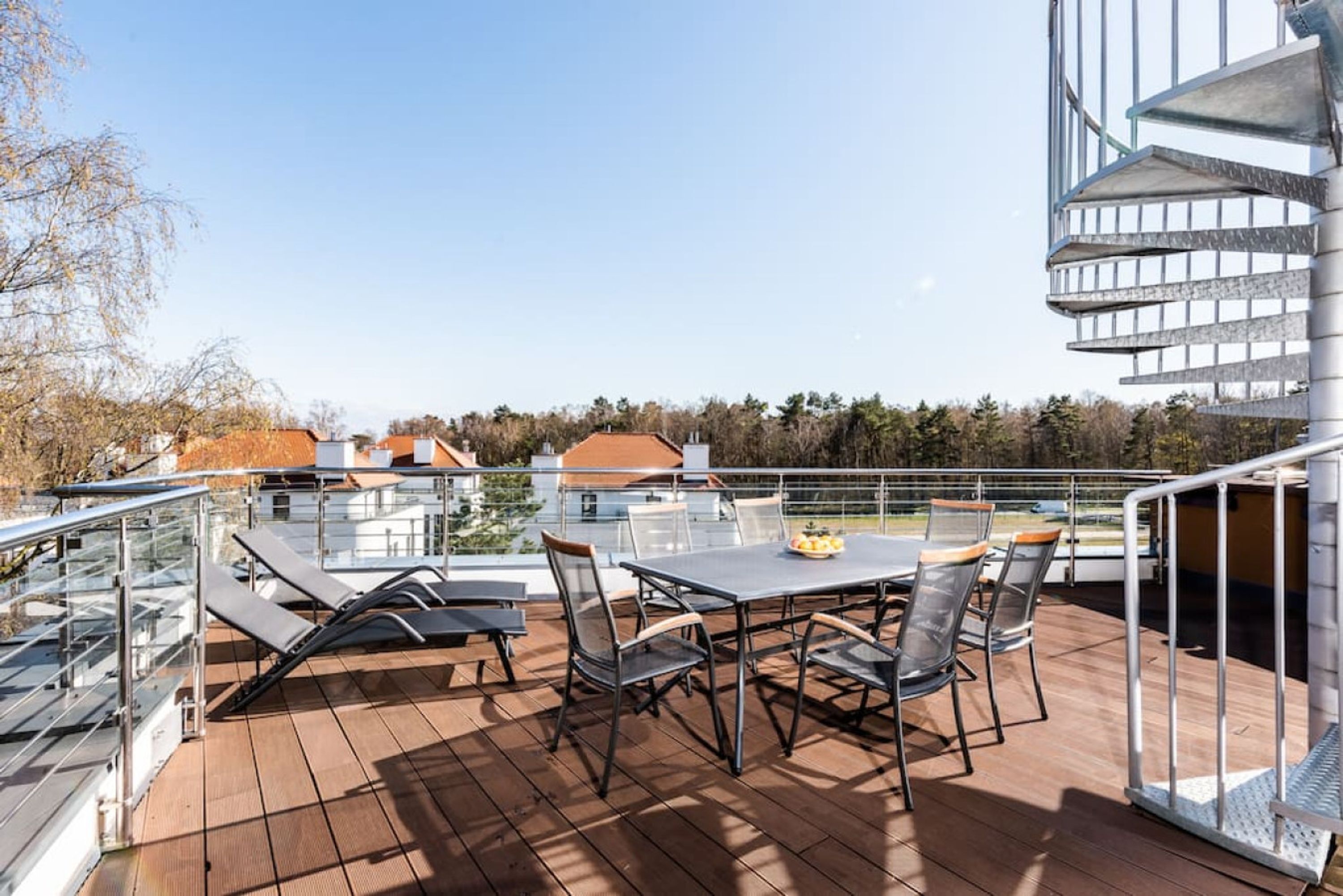 A deck with a table and chairs, overlooking a residential area with houses and trees.