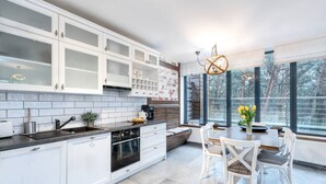 A modern kitchen with white cabinetry, a large window, and a dining area with white chairs. - Marina Dwupoziomowy Apartament Przy pla y Baltica Heaven (Trzebiatow)