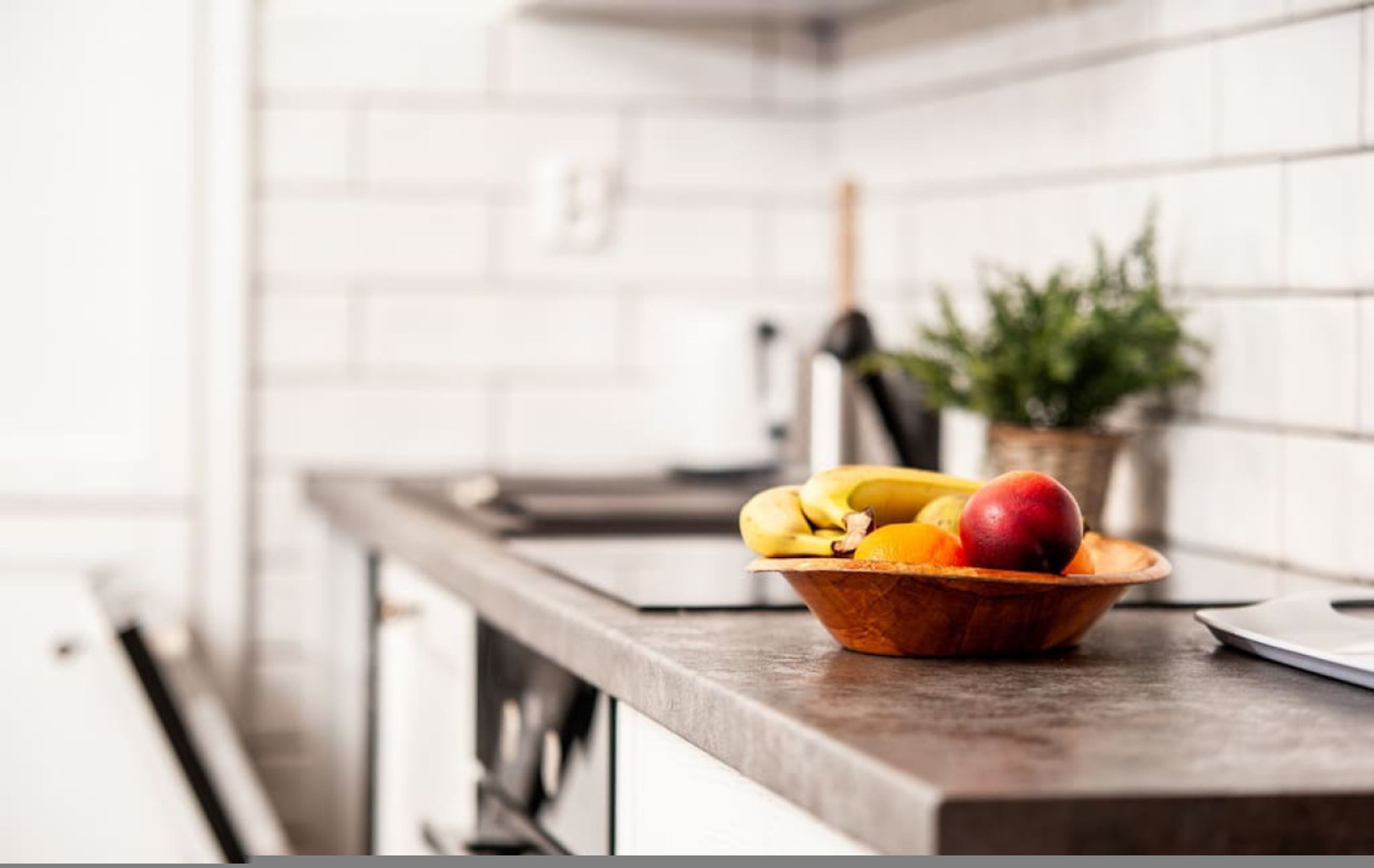 A kitchen counter with a fruit bowl containing bananas, apples, and oranges.