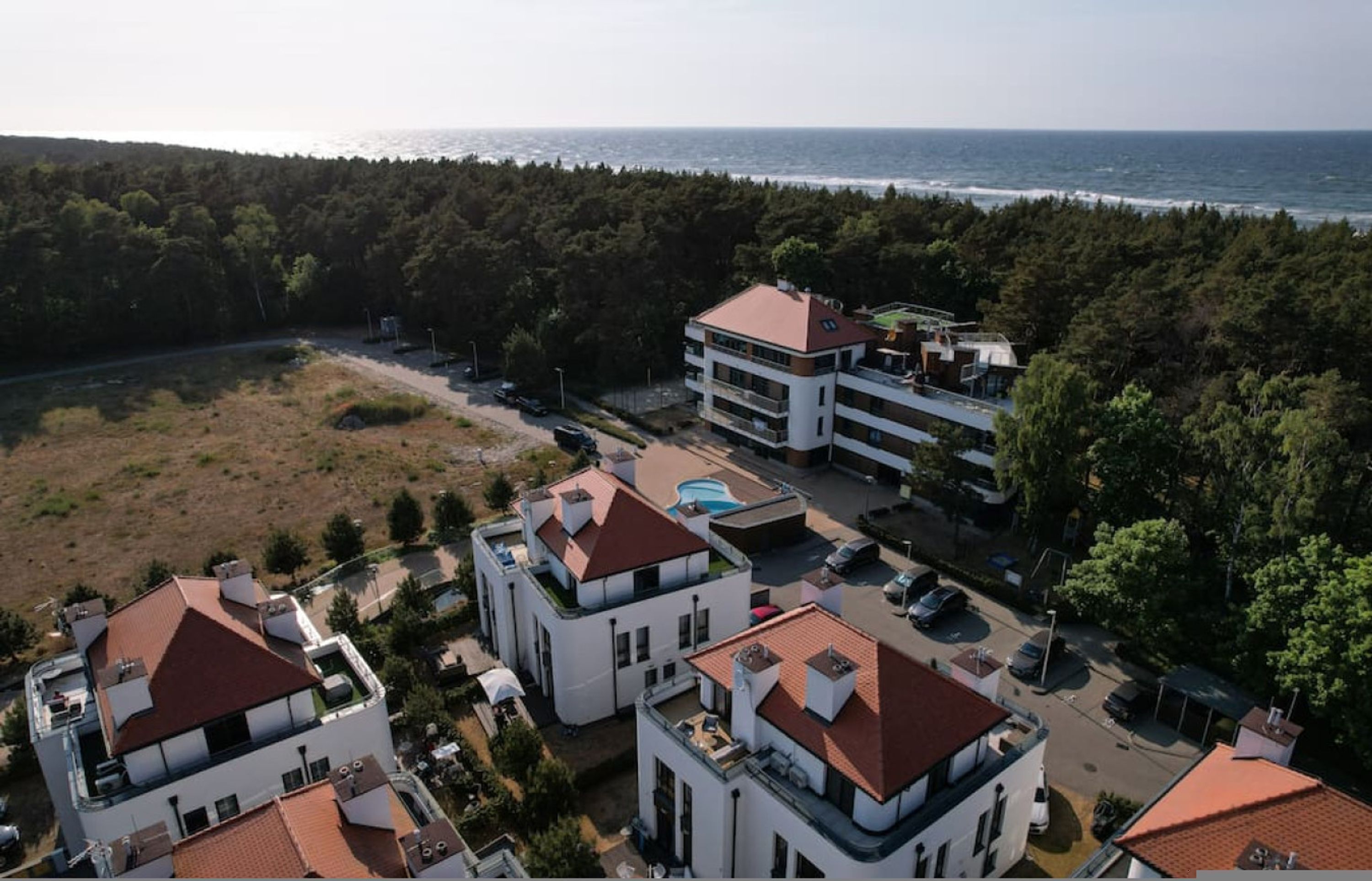 A coastal residential area with modern buildings, a swimming pool, and a view of the sea.