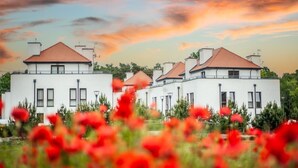 A row of modern white buildings with red roofs, surrounded by greenery and red flowers. - Jardin Taras z Ogrodem Nowoczesny Blisko Morza (Trzebiatow)