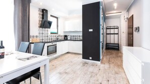 A modern kitchen with white cabinets, a black refrigerator, and a dining area with a white table and chairs. - Jardin Taras z Ogrodem Nowoczesny Blisko Morza (Trzebiatow)