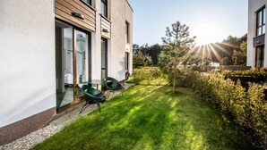 A modern building with a glass door entrance, a small outdoor seating area with chairs, and a well-maintained lawn. - Jardin Taras z Ogrodem Nowoczesny Blisko Morza (Trzebiatow)