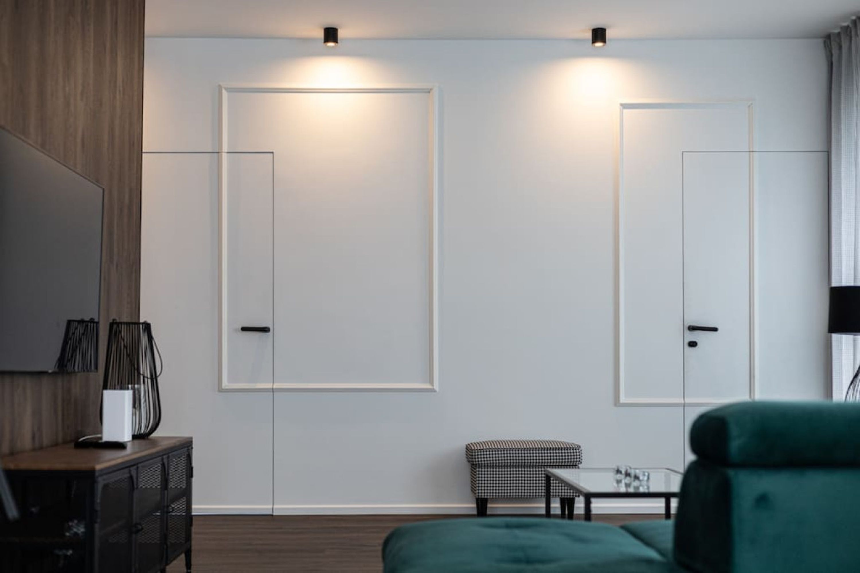 A modern room with a wooden floor, a green sofa, a small table, and two doors with light fixtures above them.