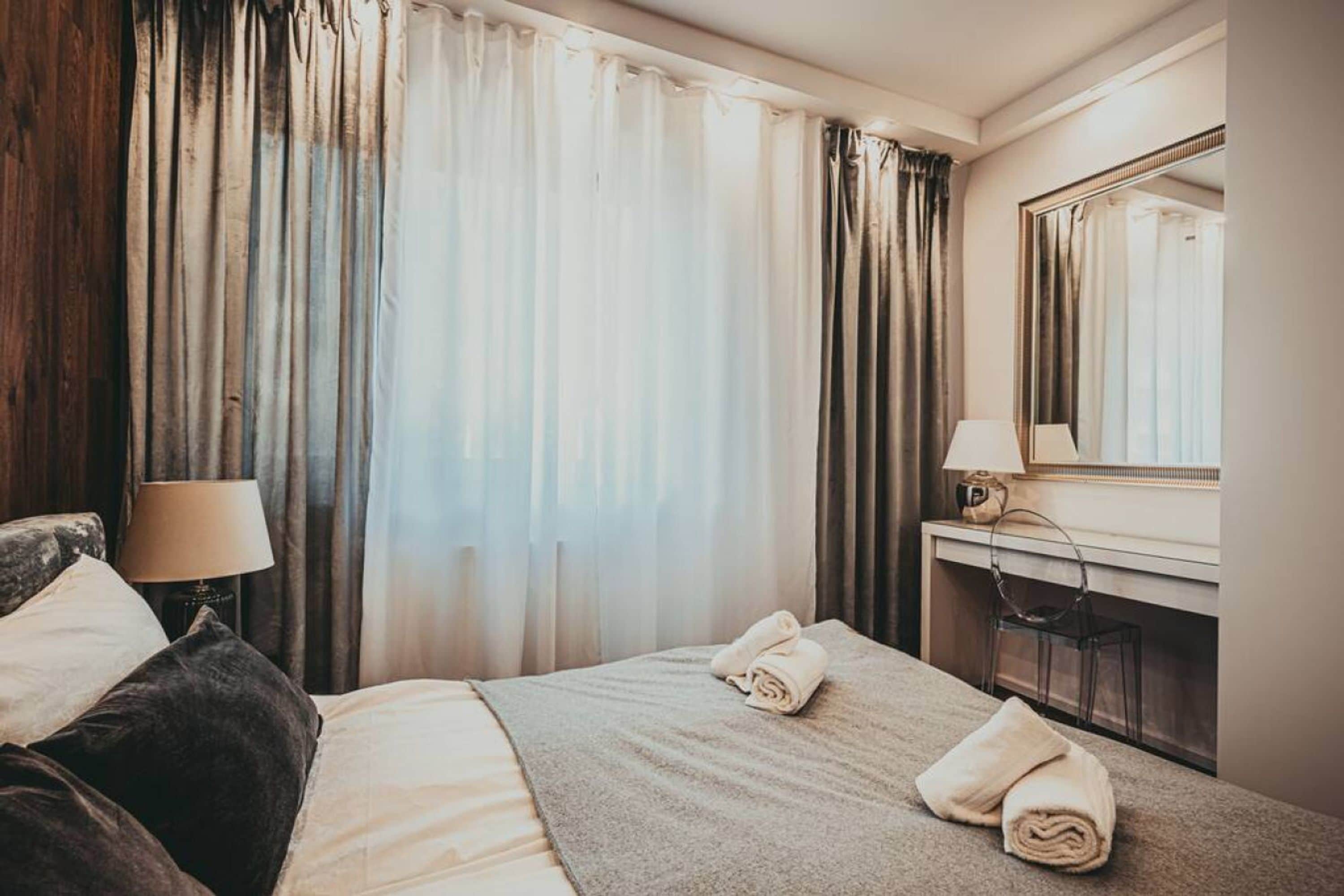 A hotel room with a bed, a desk with a lamp, a mirror, and curtains.