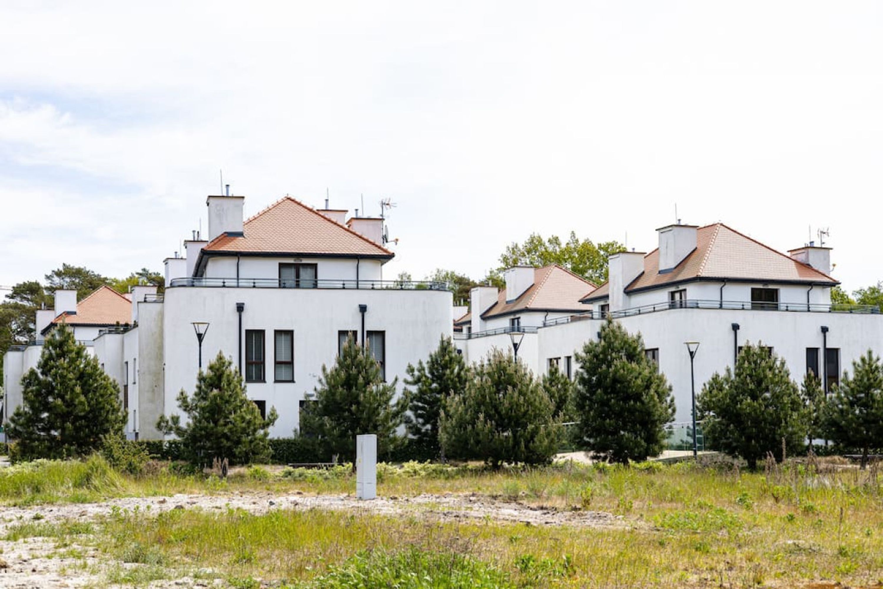 A row of white buildings with red-tiled roofs, surrounded by trees and a grassy area.