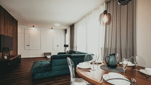 Una sala de estar moderna con piso de madera, un sofá verde, una mesa de comedor con platos y vasos blancos, y un televisor montado en la pared.
