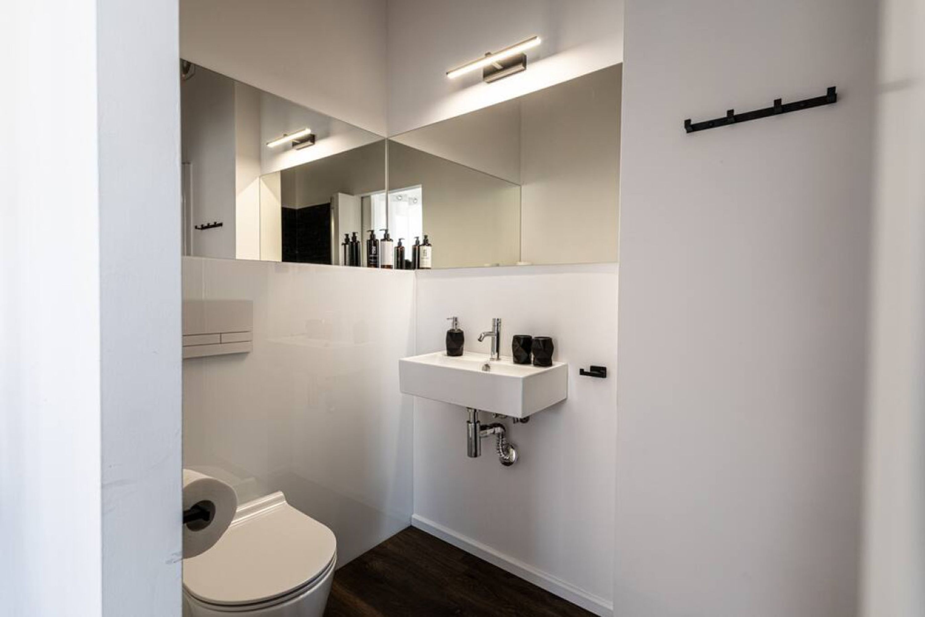 A modern bathroom with a white sink, mirror, and toilet.