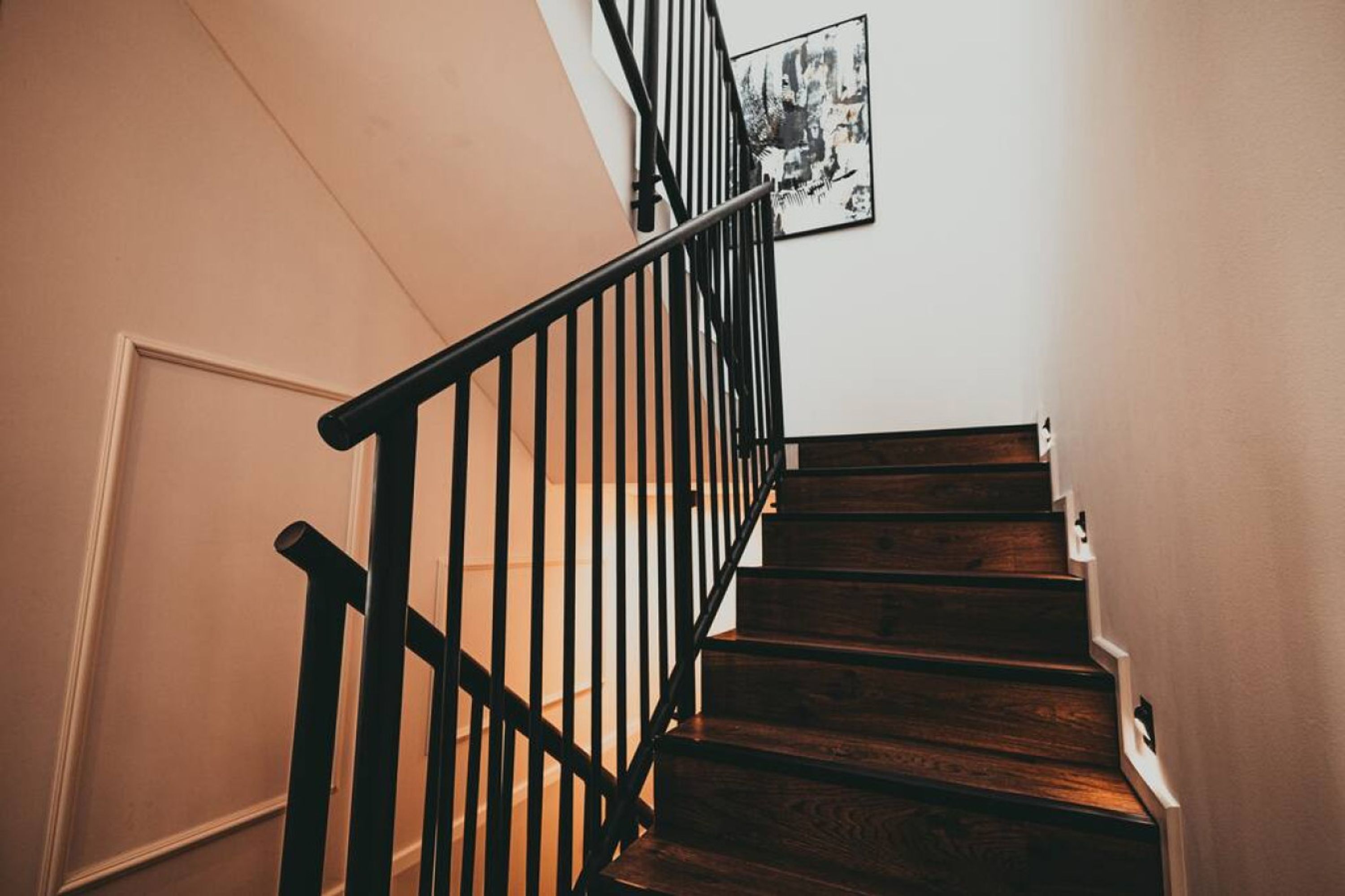 A wooden staircase with black railings and a framed picture on the wall.