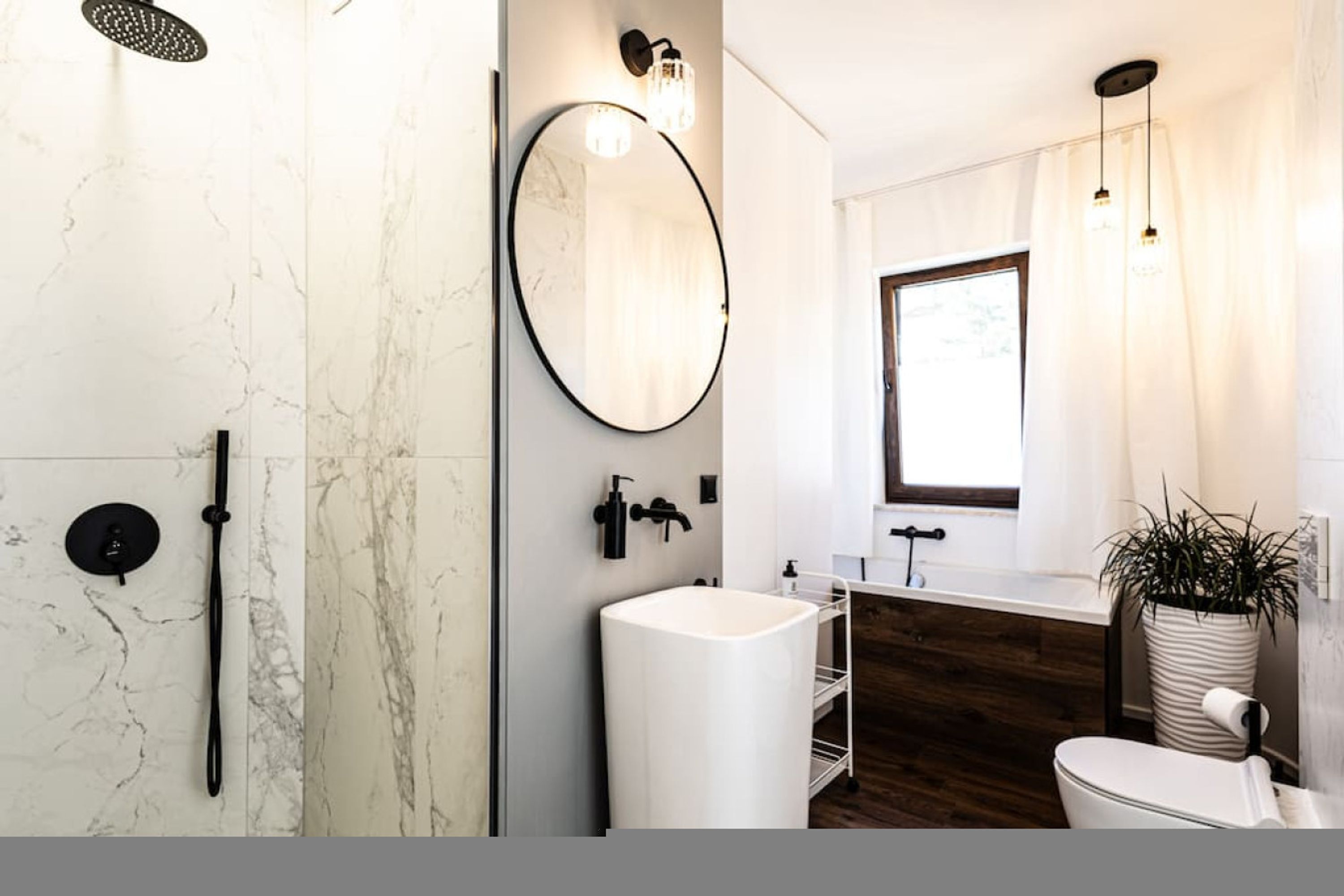 A modern bathroom with a marble wall, a freestanding sink, a large mirror, and a shower area.