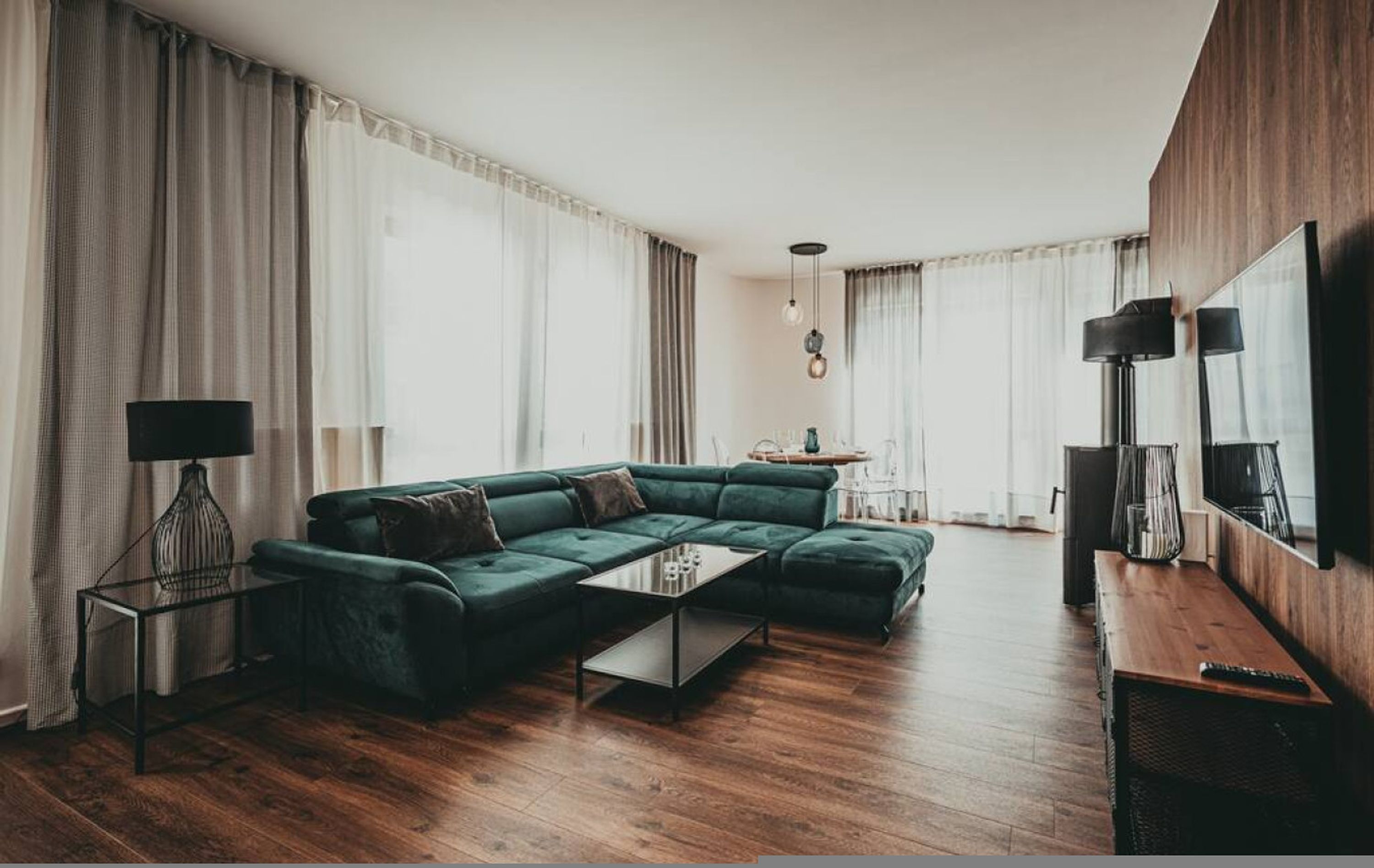 A modern living room with a green sectional sofa, a glass coffee table, and a wooden floor.