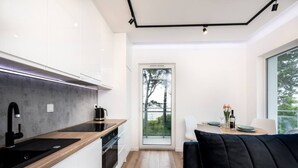 A modern kitchen with a black countertop, white cabinets, and a black sink. There is a dining area with a table and chairs, and a large window providing a view of the outdoors.