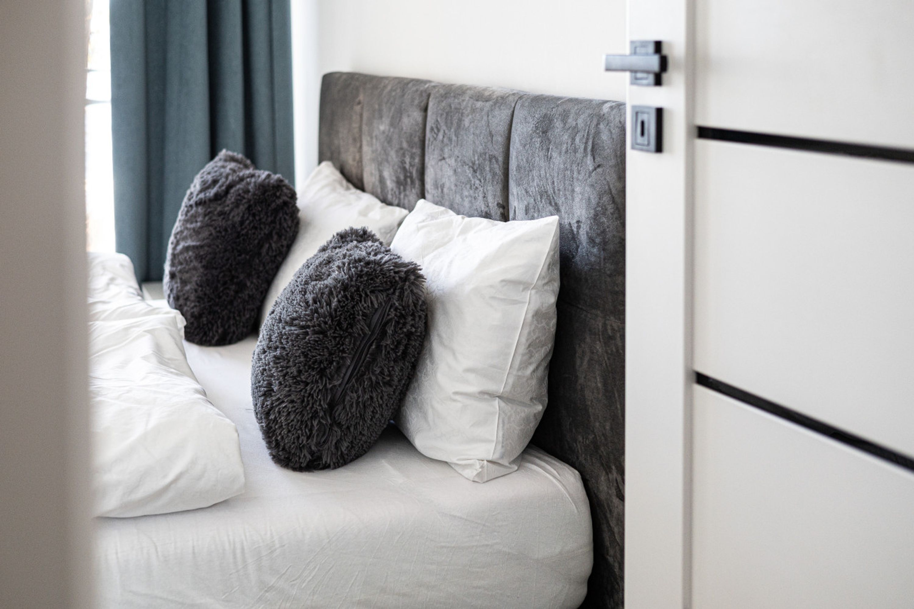 A bed with a grey upholstered headboard, white and dark grey pillows, and a white mattress.