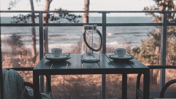 A table with two cups and a glass pitcher, set against a view of the ocean.