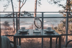 Ein Tisch mit zwei Tassen und einer Glas-Karaffe, vor dem Hintergrund eines Meerblicks.