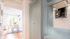 Un couloir avec une armoire en bois bleu clair, un coin repas blanc avec une table et des chaises, et un grand miroir accroché au mur.