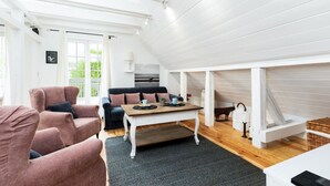 Un loft spacieux avec un plafond haut, une table à manger en bois, un canapé noir et un fauteuil rose.