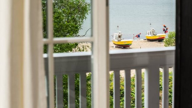 Une vue depuis une fenêtre donnant sur une plage, avec deux bateaux et un navire au loin.