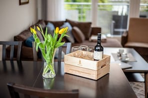 A wooden dining table with a vase of yellow tulips, a bottle of wine, and a wooden crate containing glasses and a bottle. - Santo Relaks nad Morzem Blisko Centrum i Parku (Kolobrzeg)