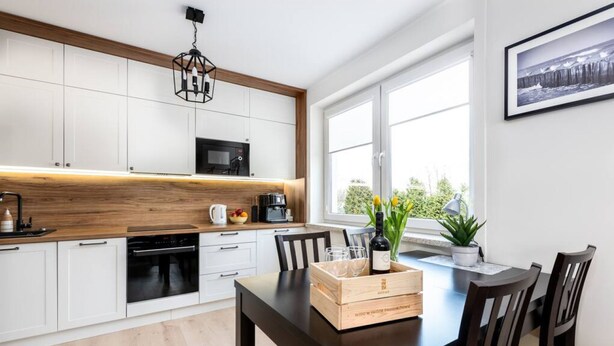 A modern kitchen with white cabinets, a wooden countertop, and a dining area with a dark table and chairs. - Santo Relaks nad Morzem Blisko Centrum i Parku (Kolobrzeg)