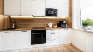 A modern kitchen with white cabinets, a wooden countertop, a built-in microwave, a coffee maker, and a dishwasher. - Santo Relaks nad Morzem Blisko Centrum i Parku (Kolobrzeg)