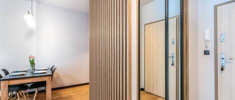 A modern room with a wooden table, chairs, a glass partition, and a door with a light switch.