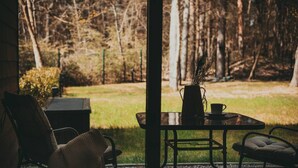 A view from inside a room with a glass door to a garden. There is a table with a vase, a cup, and a chair.