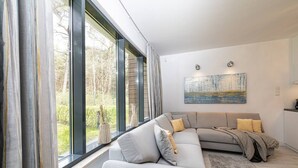 A modern living room with a large window, a sectional sofa, and a painting on the wall.