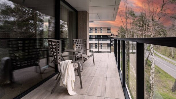 A balcony with two chairs and a small table, overlooking a road and buildings. - Natural Rogowo Rodzinny Pla a i Natura (Trzebiatow)