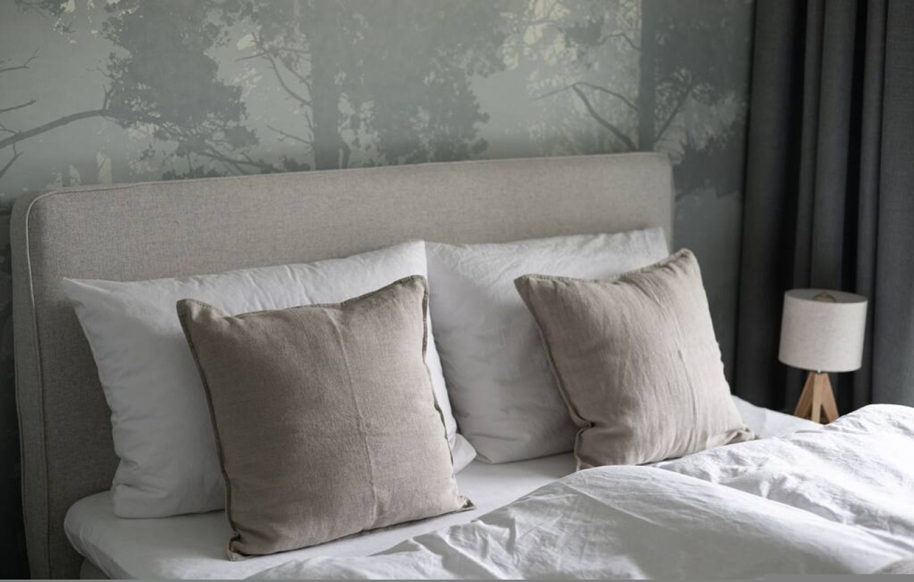 Een bed met een grijze hoofdbord, twee beige kussens en een witte deken.