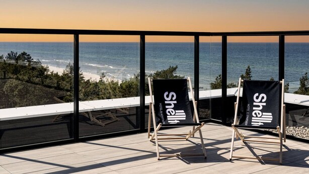 Deux chaises de plage portant la marque « Shell Hotel » sont placées sur un balcon donnant sur l’océan.