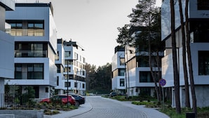 Une rue urbaine moderne, bordée d’immeubles contemporains, avec un cheminement piétonnier sinueux et des voitures garées.